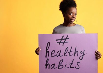 Portrait of a woman holding a healthy habits sign, set against a vibrant yellow background.