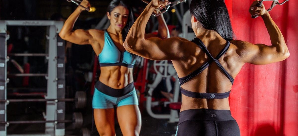 Strong female bodybuilder doing cable workout in a gym with mirror reflection.